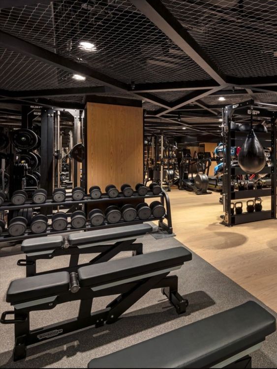 an empty gym with rows of exercise benches and weight machines on the floor, in front of a row of black dumbbells