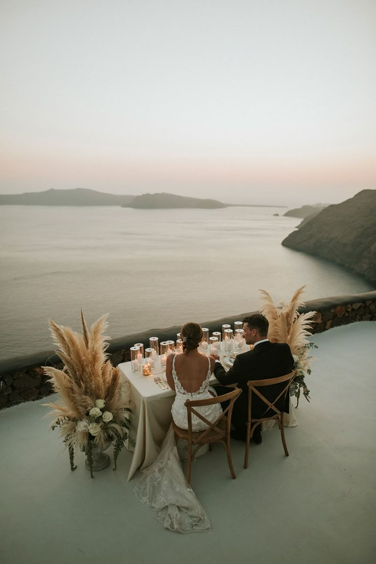 a bride and groom sitting at a table overlooking the ocean