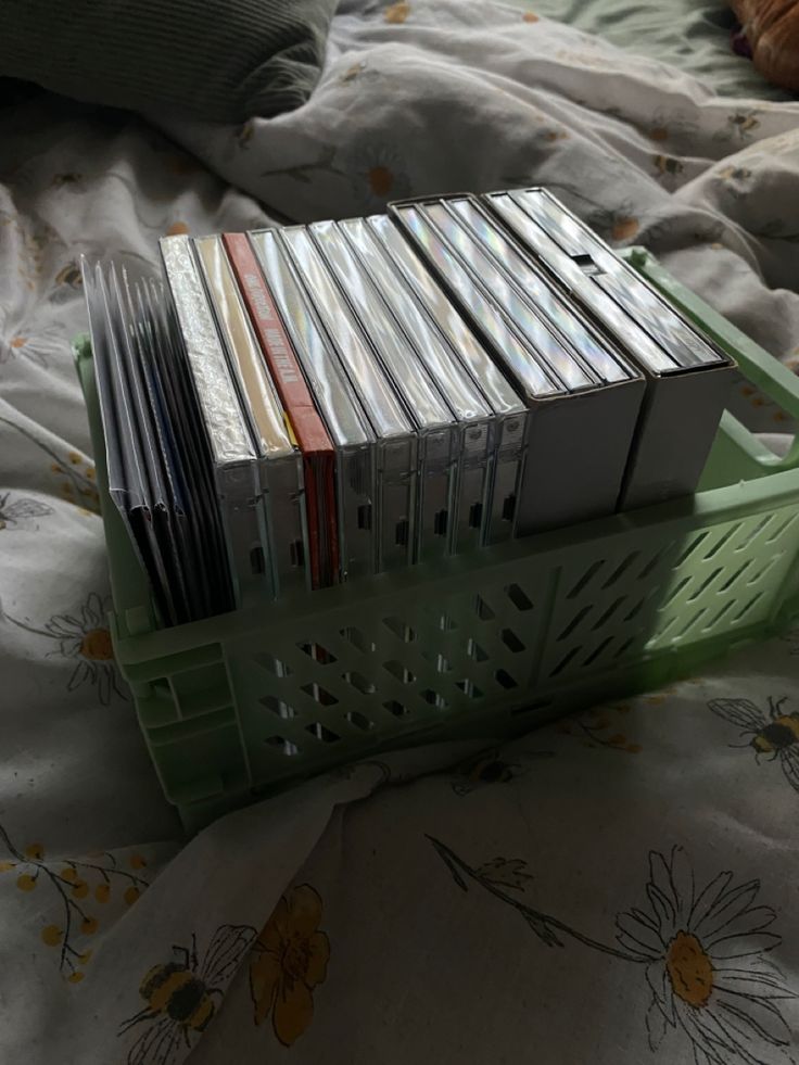 a stack of cds sitting on top of a bed next to a basket filled with them