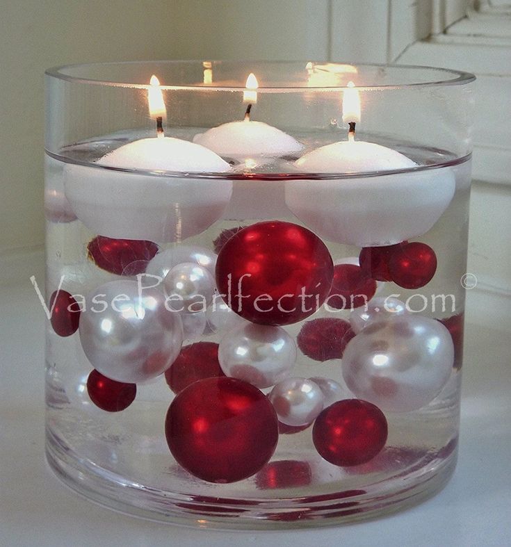 two candles are in a glass bowl with red and white ornaments on the bottom one candle is lit