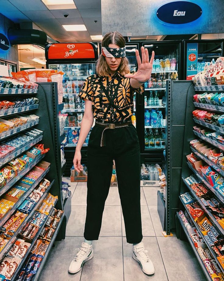 a woman standing in front of a store filled with shelves and food items, making the peace sign