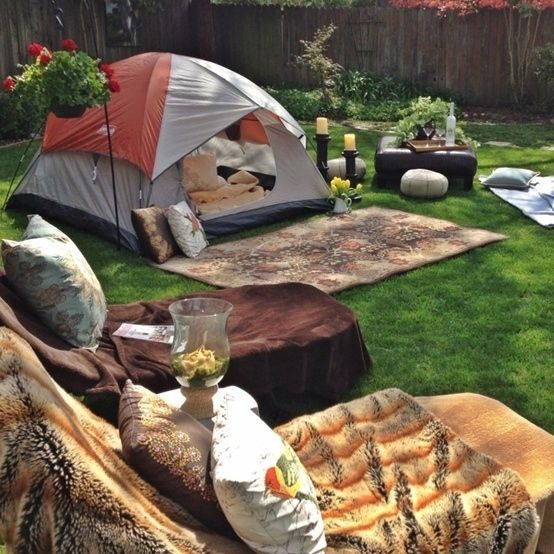 a tent set up in the middle of a yard with blankets and pillows on it