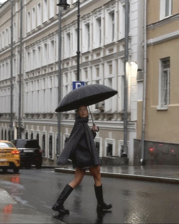 a woman walking down the street in the rain with an umbrella over her head and black boots