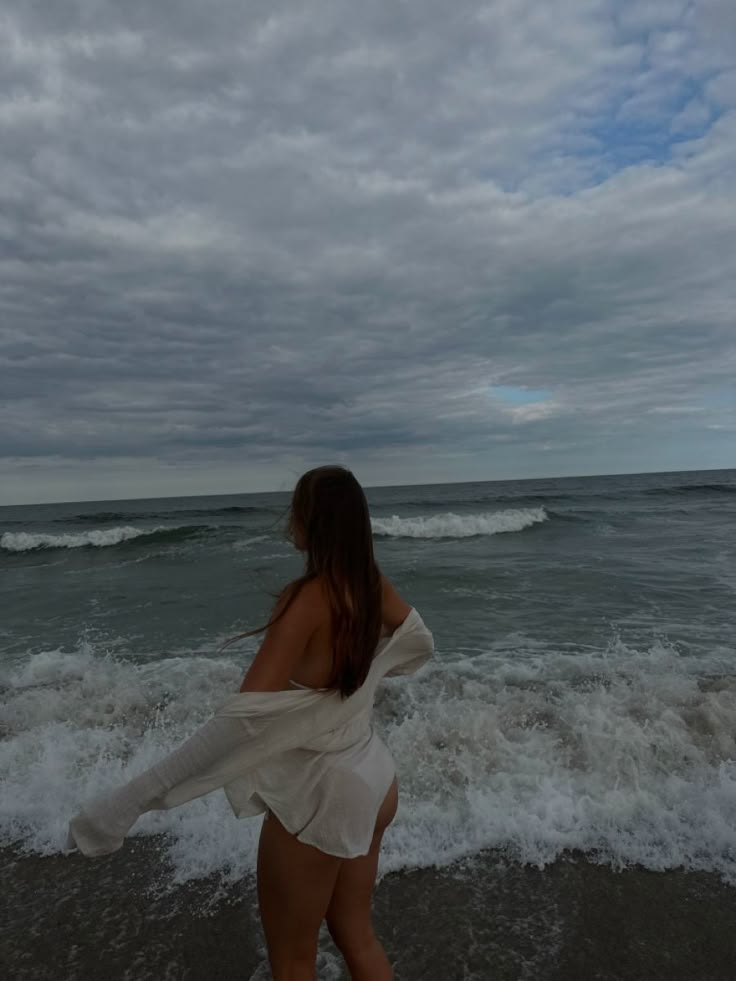 a woman in a white dress walking on the beach