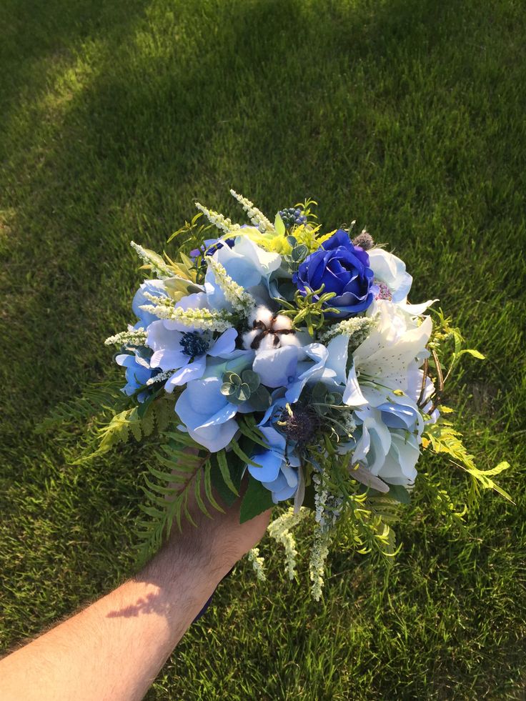 a hand holding a blue and white bouquet on top of green grass in the sun