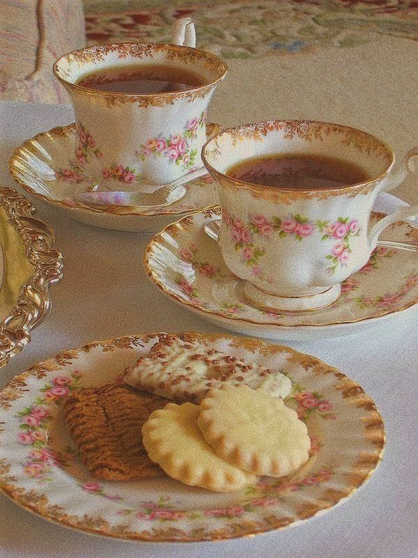 two tea cups and saucers filled with cookies on a white tablecloth covered table