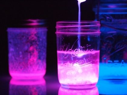 two jars filled with liquid sitting next to each other on top of a table covered in blue and pink lights