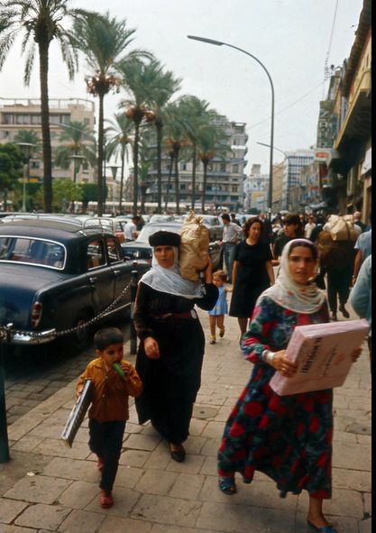 two women and a child are walking down the street in front of old fashioned cars