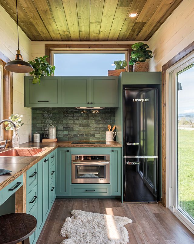 a kitchen with green cabinets and wood floors, along with an open door leading to the outside