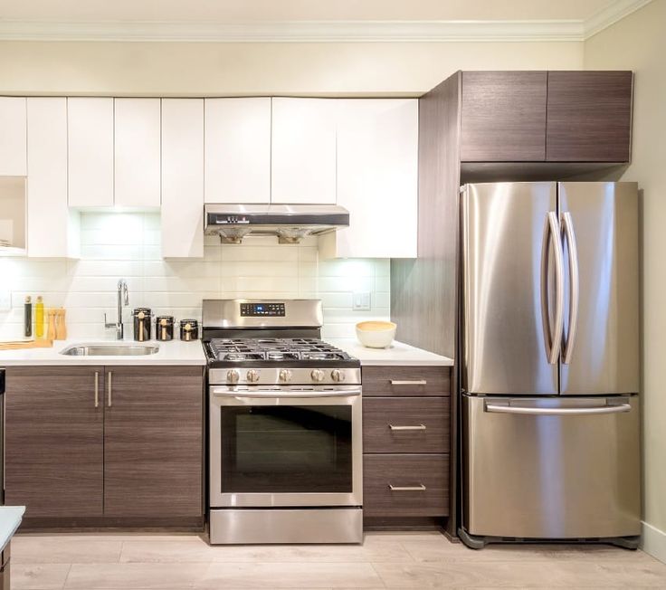 a stainless steel refrigerator and stove in a small kitchen with white counter tops, cabinets, and drawers