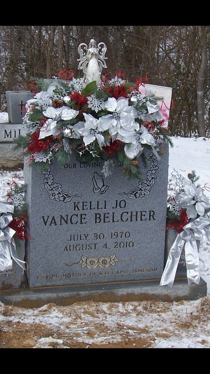 a headstone with flowers and ribbons on it in the middle of a snow covered field