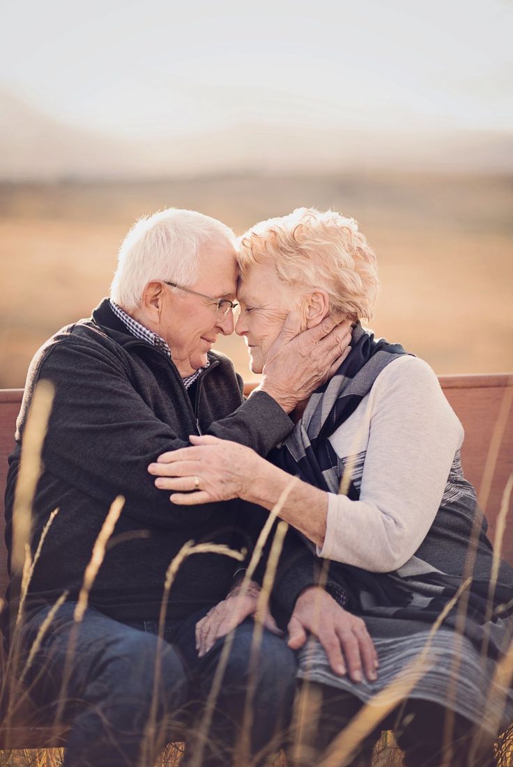 an older couple sitting on a bench in the middle of a field hugging each other