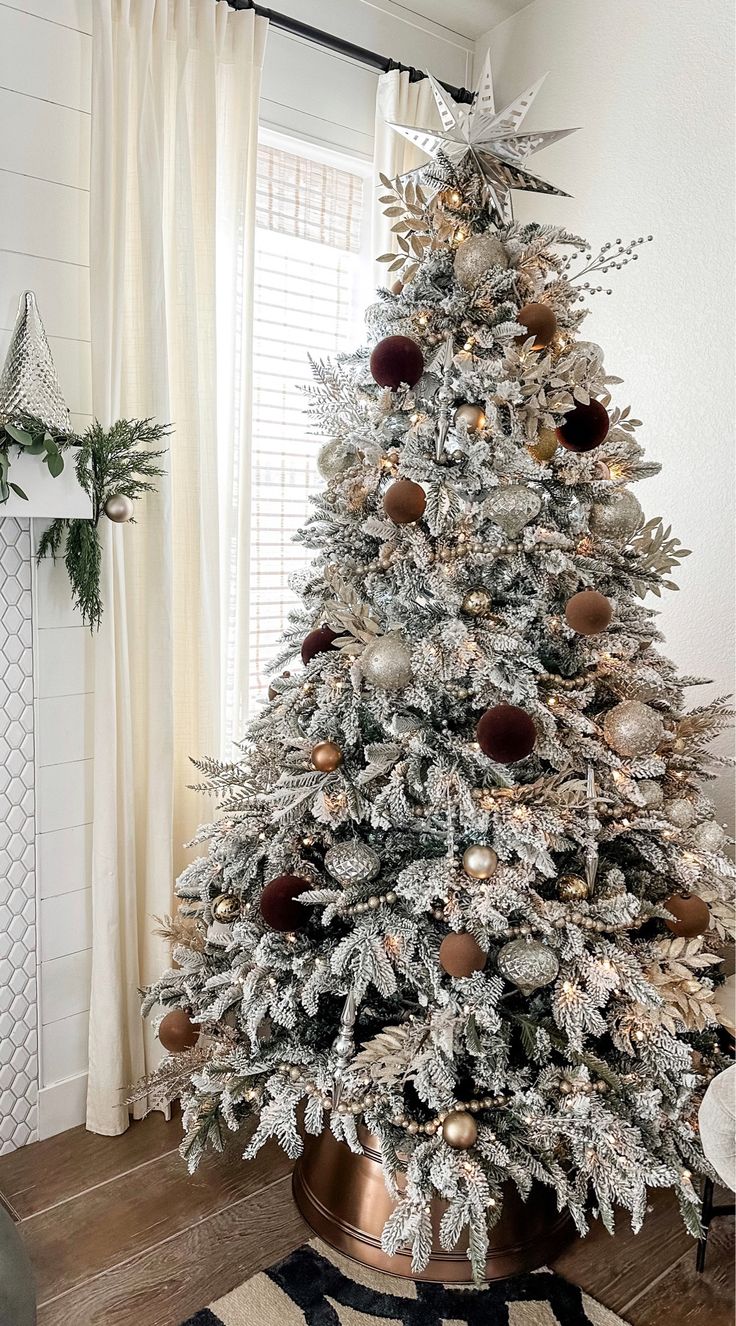 a white christmas tree with gold and silver ornaments on it in a living room next to a window