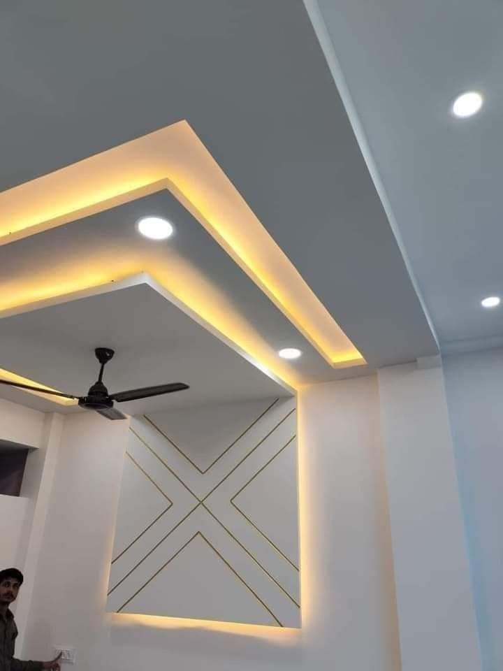 a man standing next to a ceiling fan in a room with white walls and lights