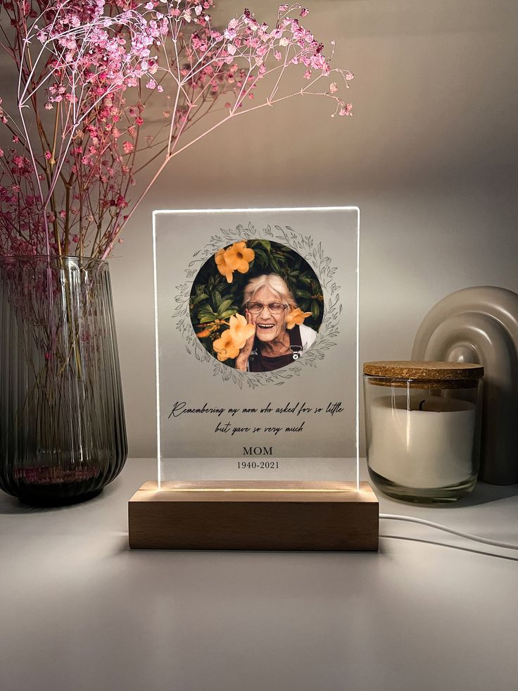 a vase filled with flowers next to a photo on a wooden stand and a candle