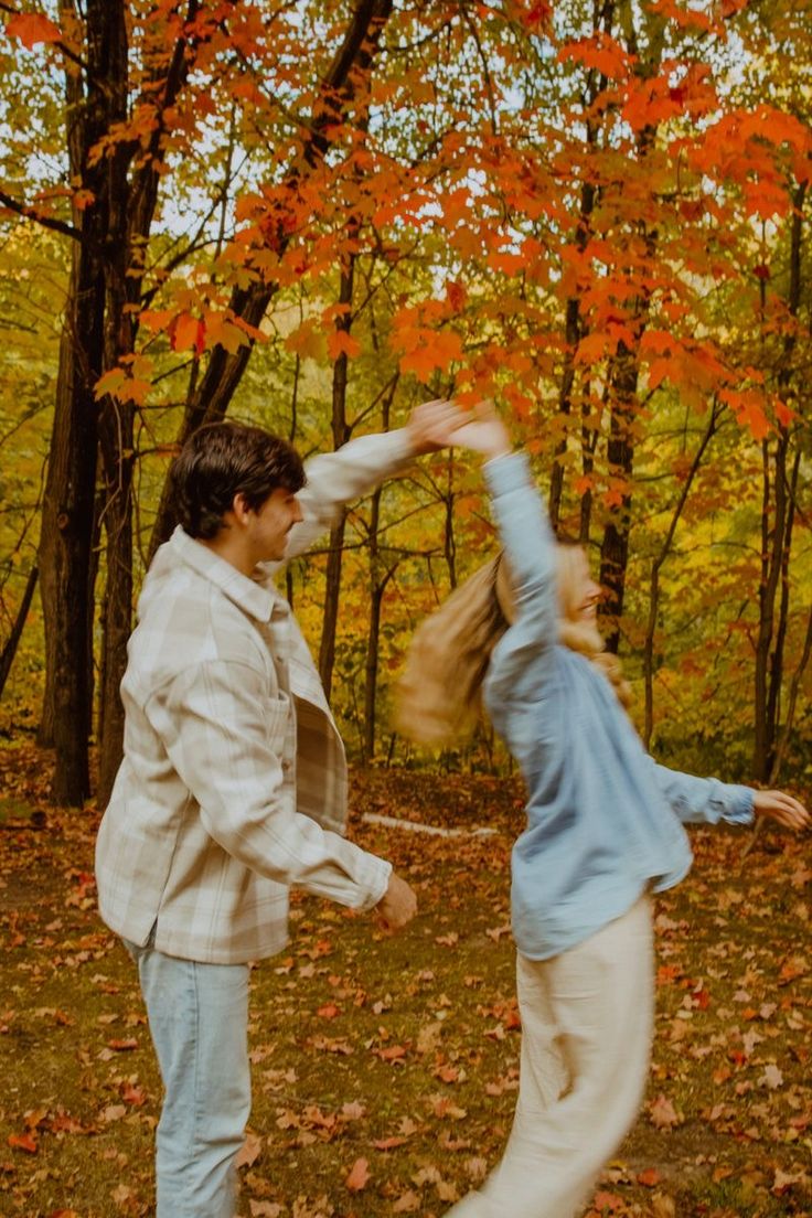 two people are dancing in the woods with leaves on the ground and trees behind them