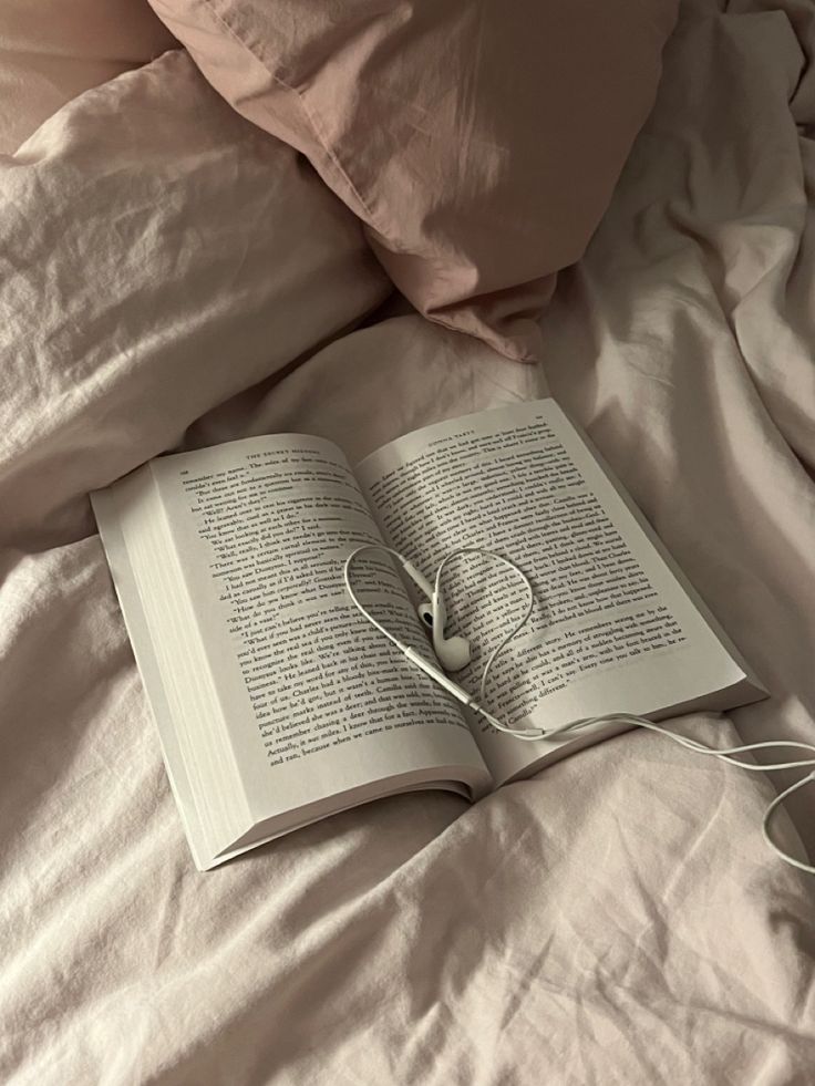 an open book on top of a bed with white sheets and pink pillowcases