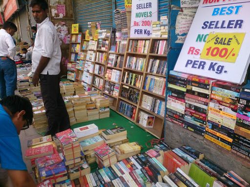 people are browsing books at an outdoor book market in india, with signs on the shelves