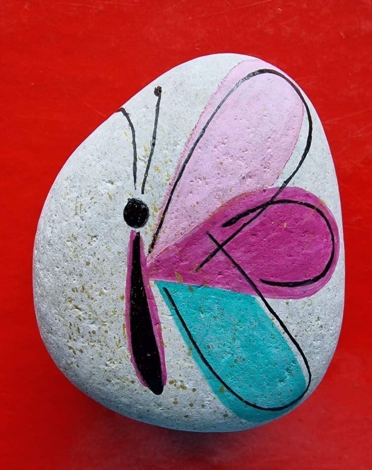 a painted rock sitting on top of a red floor next to a white and blue butterfly