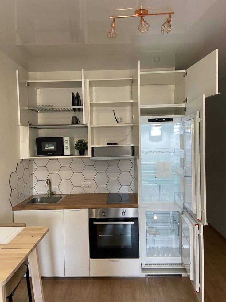 an empty kitchen with white cabinets and wood flooring is pictured in this image, the refrigerator has its door open