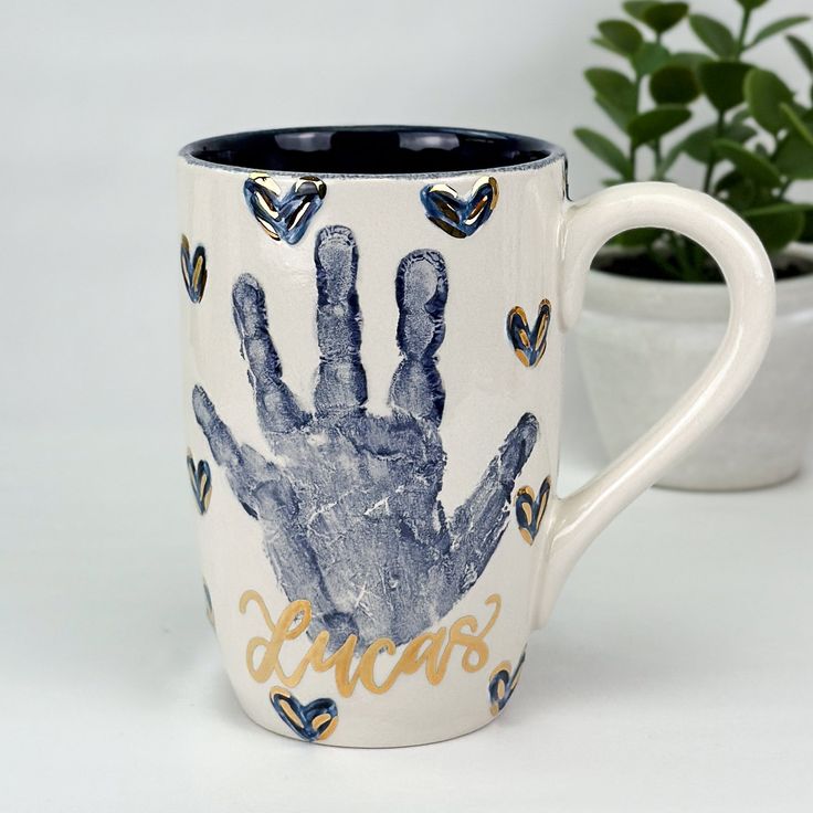 a coffee cup with a hand print on it and a potted plant in the background