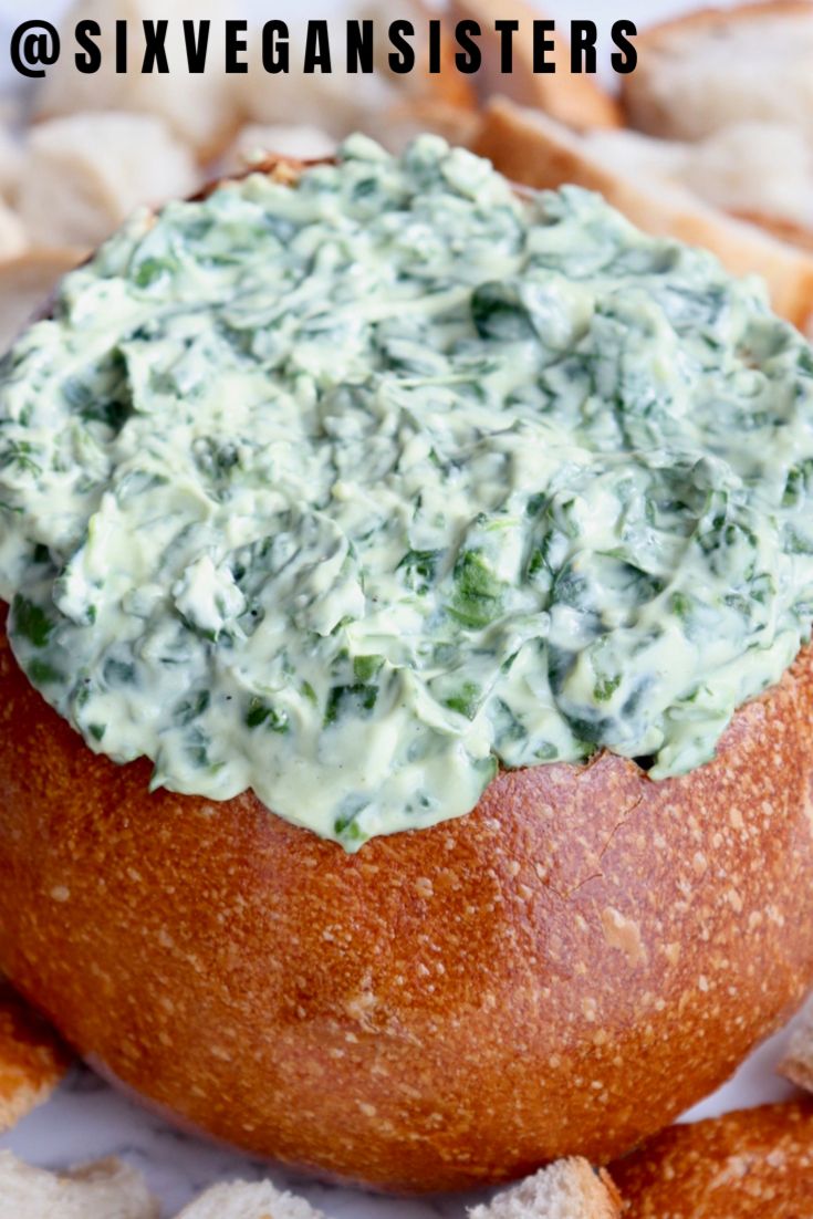 a bread bowl filled with spinach dip surrounded by crackers