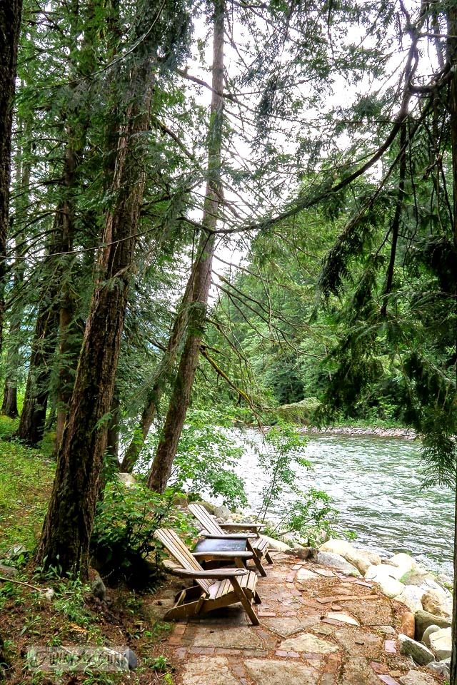 two wooden benches sitting on top of a stone walkway next to a river in the woods