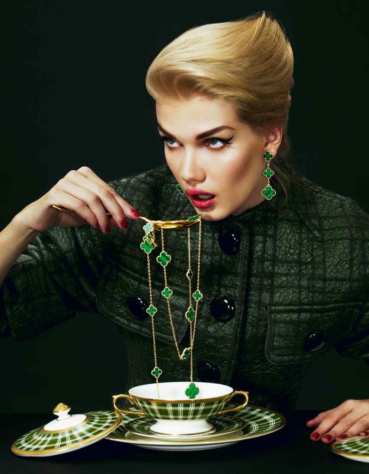 a woman is holding a necklace over a teacup and saucer with jewelry on it