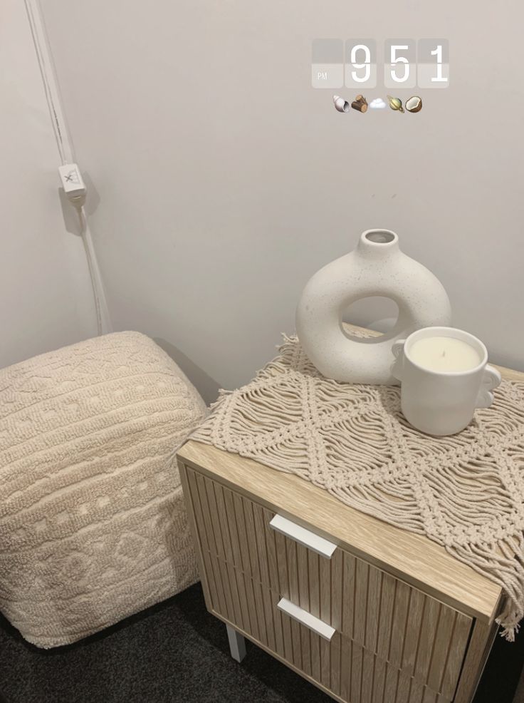 a white vase sitting on top of a wooden table next to a bed and night stand