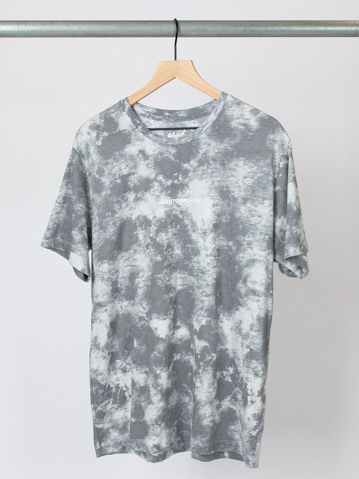 a gray and white tie dye t - shirt hanging on a hanger with clothes pins