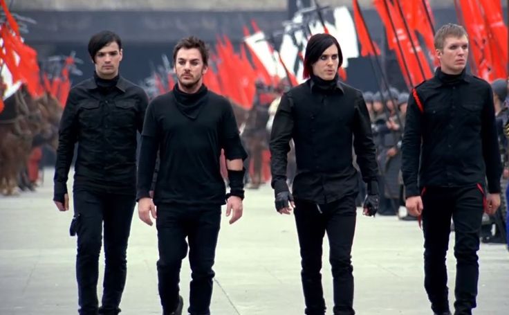 three men in black outfits walking down the street with red flags on either side of them