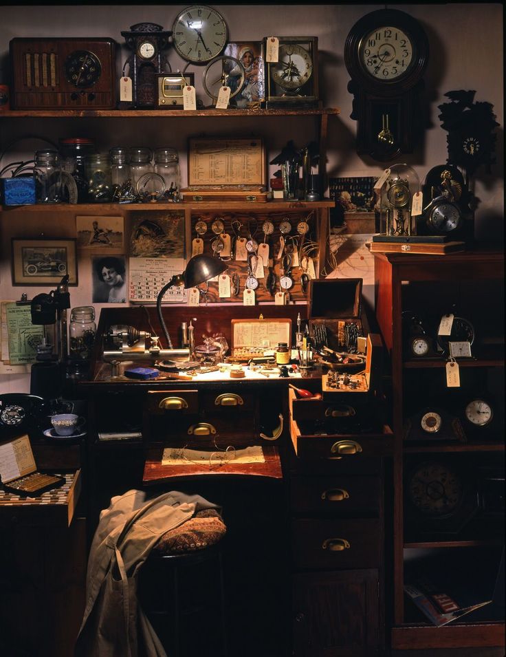 an old fashioned desk with lots of clocks on the wall above it and shelves below