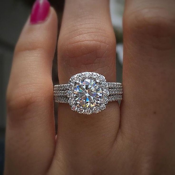 a woman's hand with a diamond ring on top of her finger and the other hand holding an engagement ring