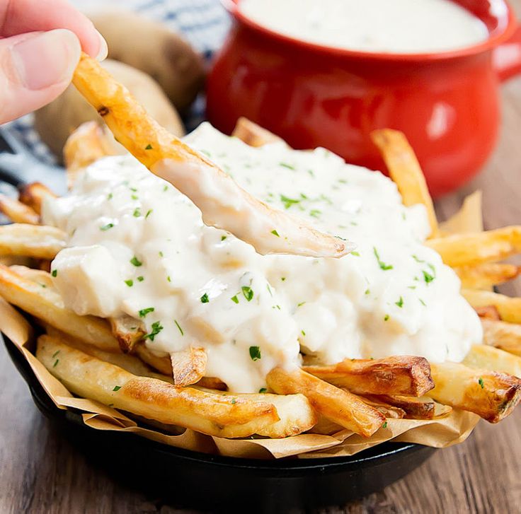 a hand holding a piece of french fries with ranch dressing on top in a black bowl