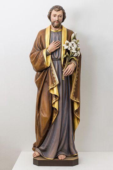 a statue of jesus holding a bouquet of flowers on a white surface with a wall behind it