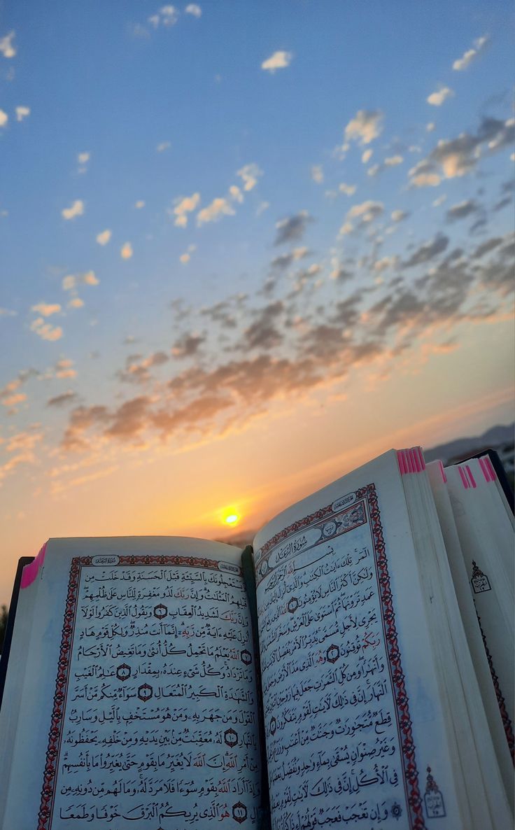 an open book sitting on top of a table next to a sky filled with clouds