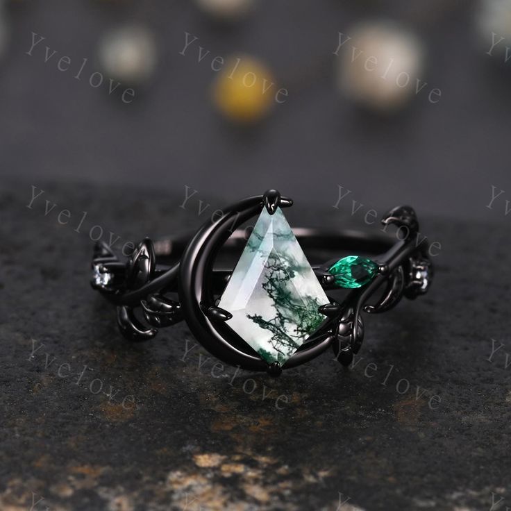 a ring with a green stone in the middle on top of a black surface next to other jewelry items