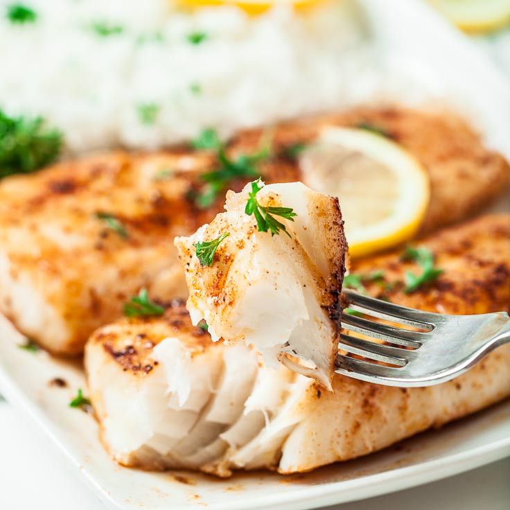 a piece of fish on a white plate with a fork in it and lemon wedges