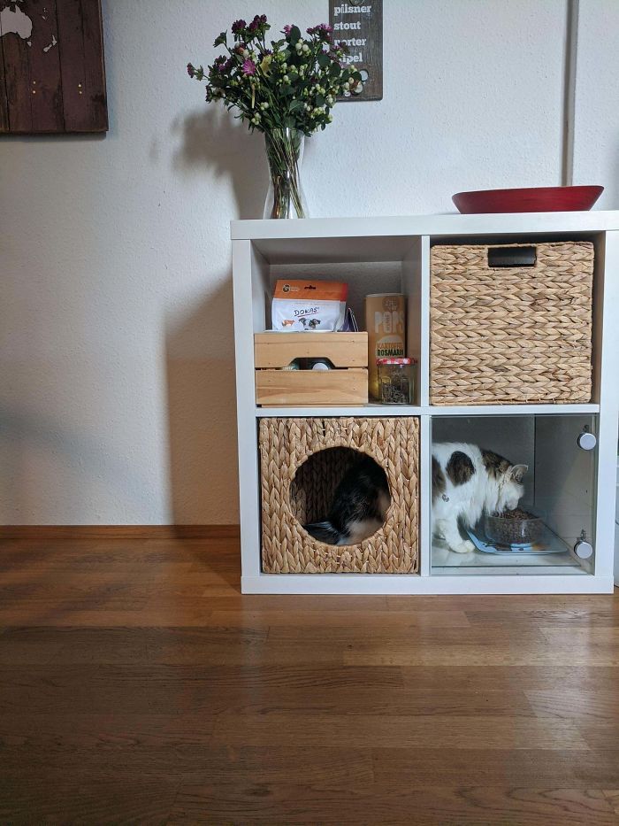 the cat is laying in the basket on the shelf next to the flower vase and other items