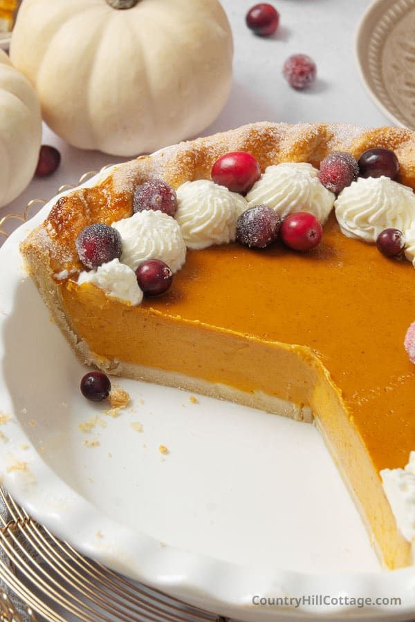 a slice of pumpkin pie with whipped cream and cranberries sits on a plate