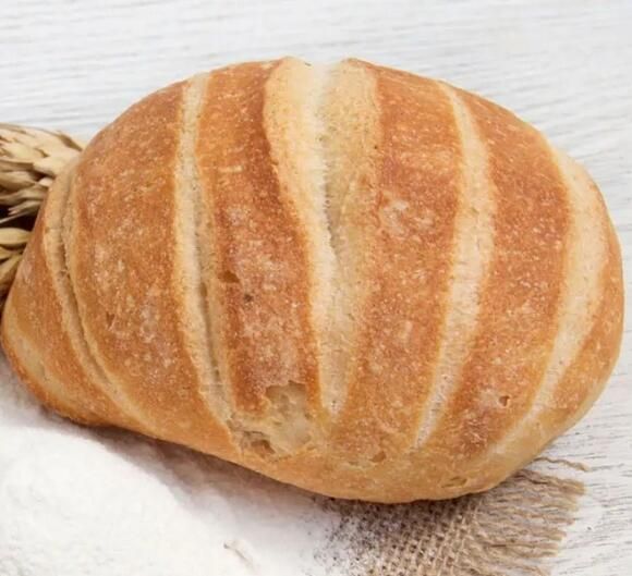 a loaf of bread sitting on top of a piece of white paper next to a wheat stalk