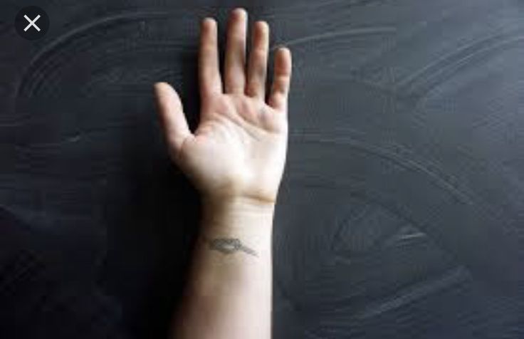 a person's hand with a small tattoo on their left wrist, against a black background