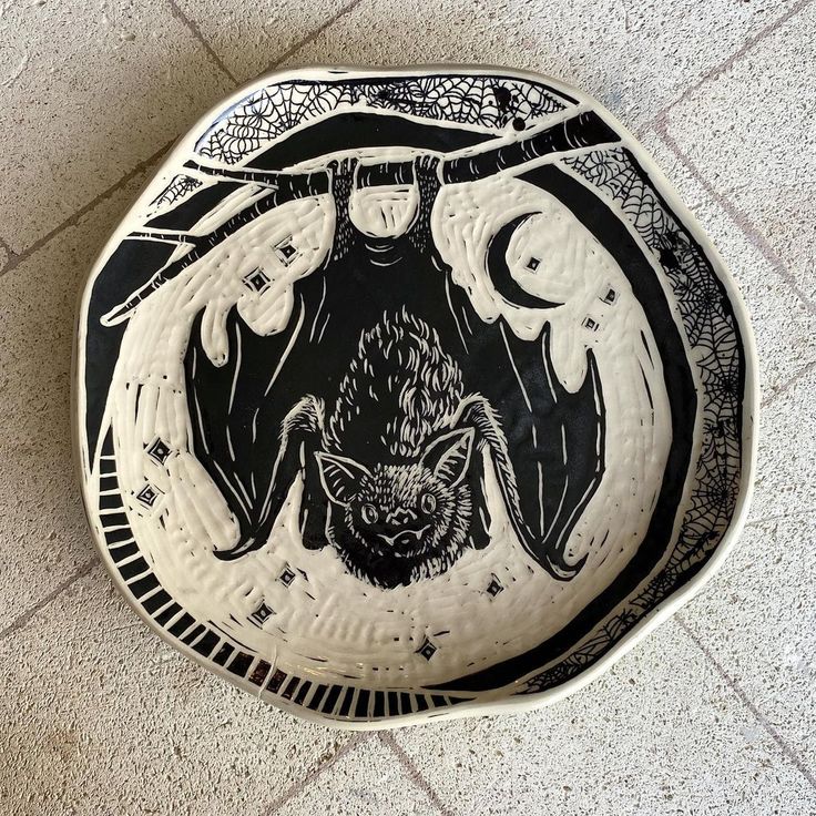 a black and white plate with a bat painted on it's side sitting on the floor