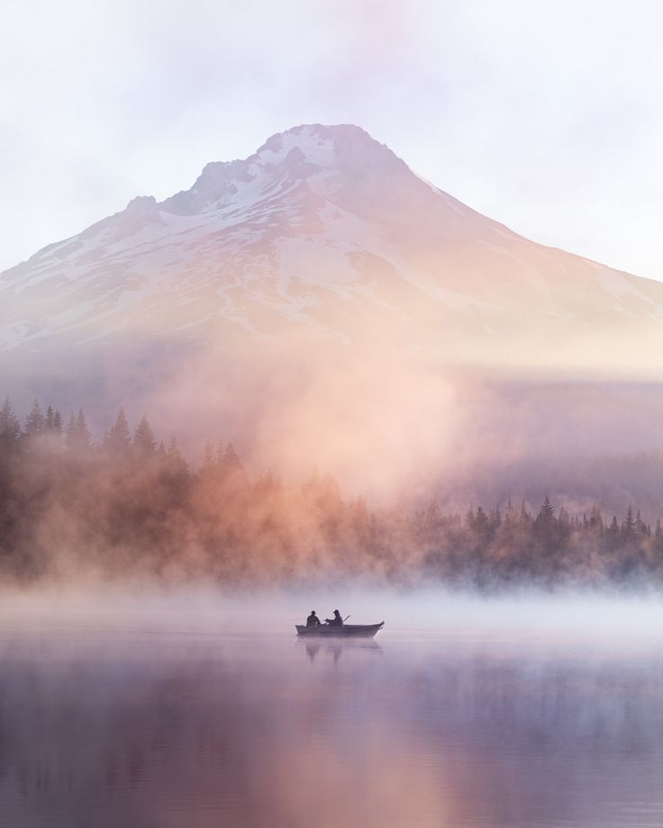 two people in a small boat on a lake with mountains in the backgroud