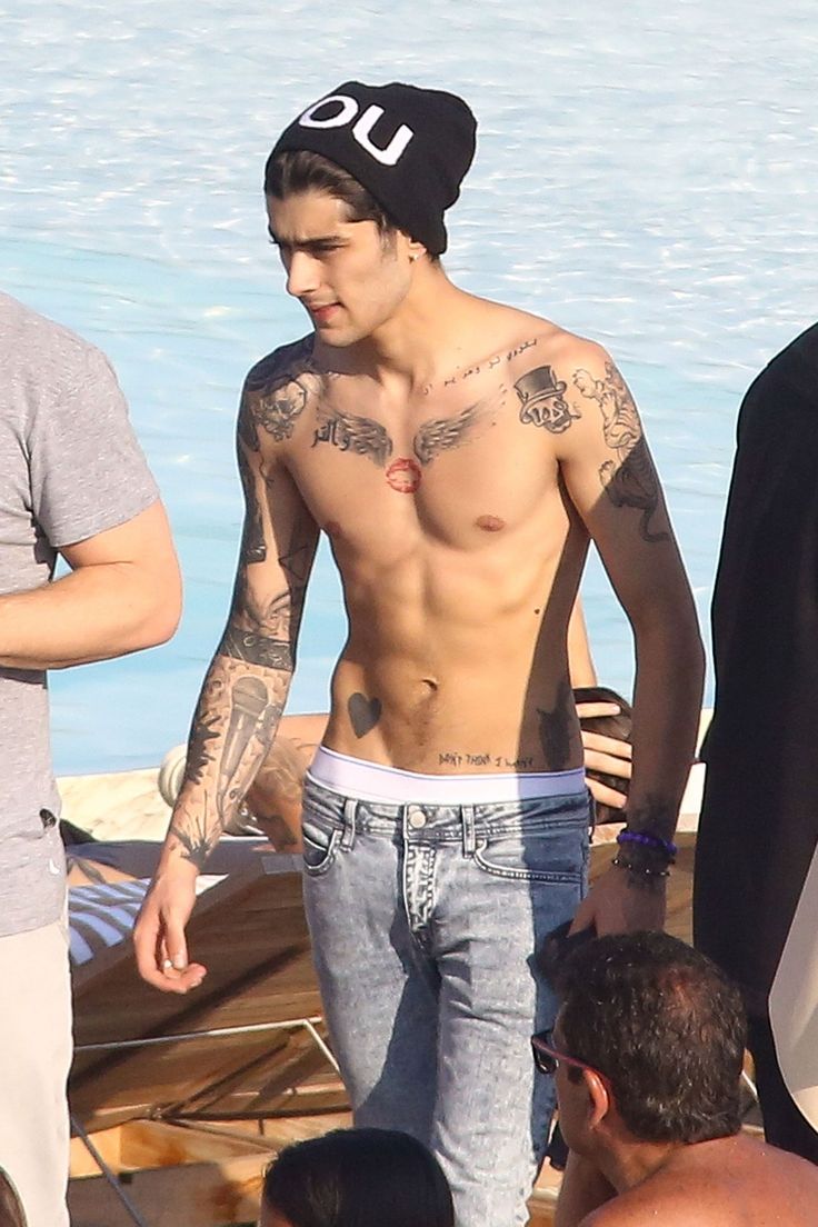 a shirtless man standing next to other men on the beach with water in the background