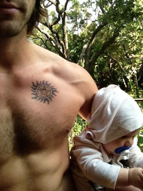 a man with a sun tattoo on his chest holding a small child in his arms