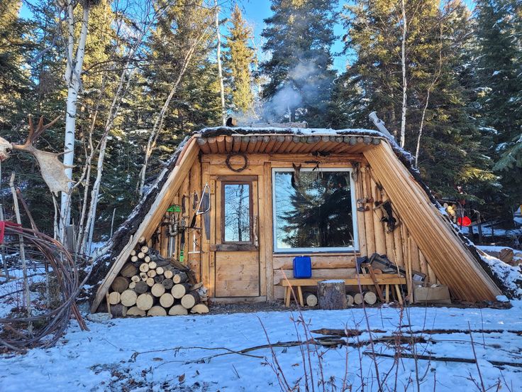 a small wooden cabin in the woods with snow on the ground and trees around it