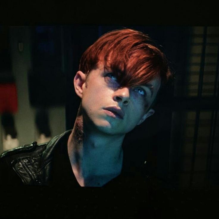 a young man with red hair and blue eyes stares into the distance in a dark room