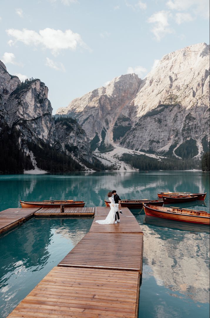 a bride and groom standing on a dock in front of some boats at the lake