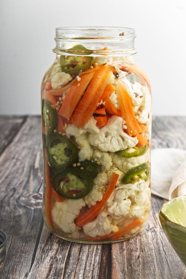 a mason jar filled with vegetables on top of a wooden table